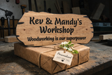 Wooden sign with 'Kev & Mandy's Workshop' and 'Woodworking is our superpower' text, wrapped gift with tag in workshop setting.