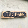 Rustic carved oak house sign with raised lettering mounted on exterior wall