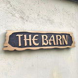 Rustic carved oak house sign with raised lettering mounted on exterior wall
