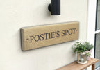 Wooden sign with 'POSTIE'S SPOT' on a wall next to a plant and lantern.
