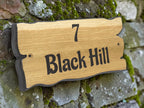 Wooden house number sign with '7 Black Hill' engraved on a stone wall.