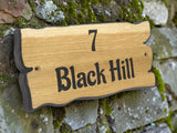Wooden house number sign with '7 Black Hill' engraved on a stone wall.