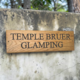 Engraved oak glamping site sign mounted on rustic stone wall outdoors