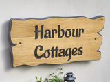 Large personalised oak house name sign Harbour Cottages mounted above bench with lantern and plant