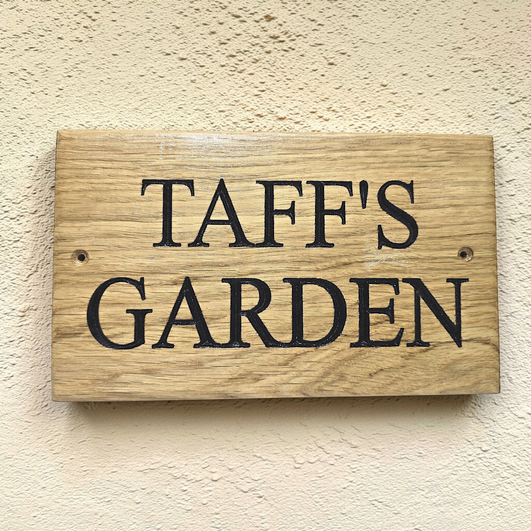 Personalised oak garden sign with deep engraved lettering mounted on exterior wall