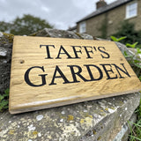 Rustic oak garden plaque resting on natural stone wall in countryside setting