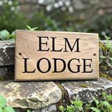 Personalised oak lodge sign displayed on garden stone wall with greenery background