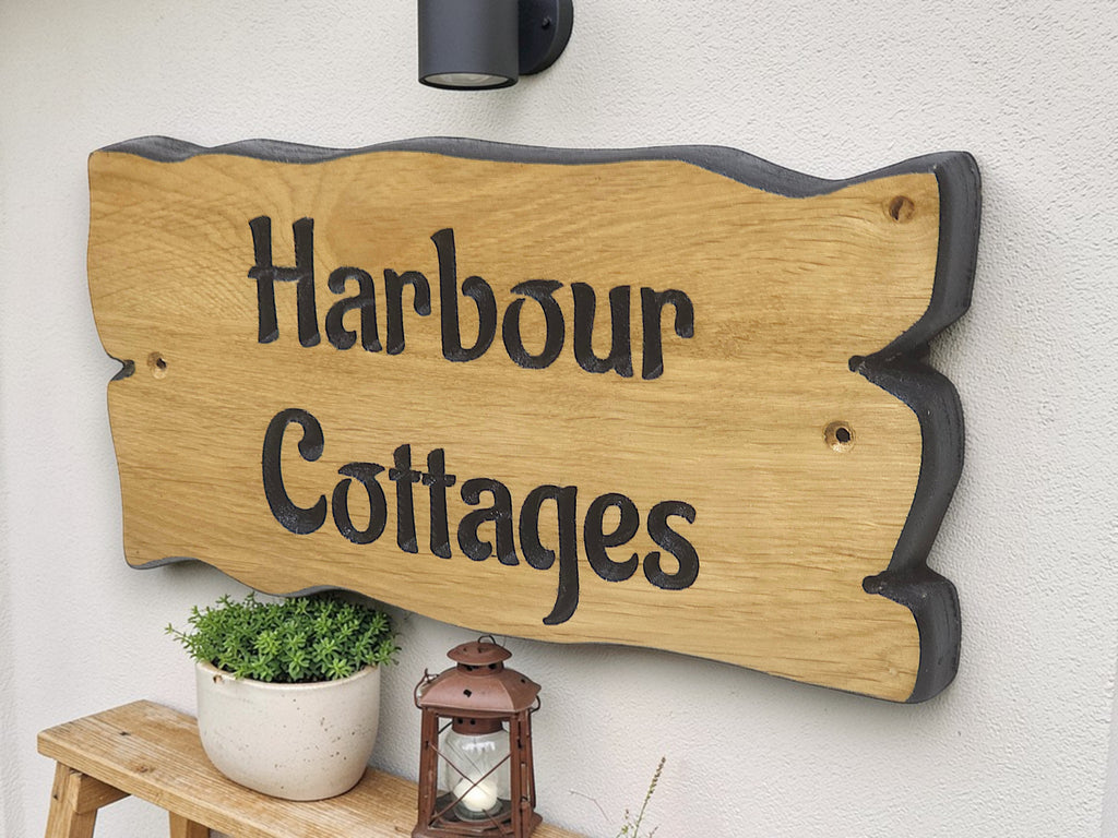 Wooden sign with 'Harbour Cottages' on a white wall with a plant and lantern.