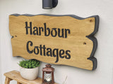 Wooden sign with 'Harbour Cottages' on a white wall with a plant and lantern.