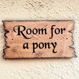 Wooden sign with 'Room for a pony' text on a textured wall.