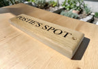 Wooden sign with 'POSTIE'S SPOT' engraved on a wooden surface outdoors.